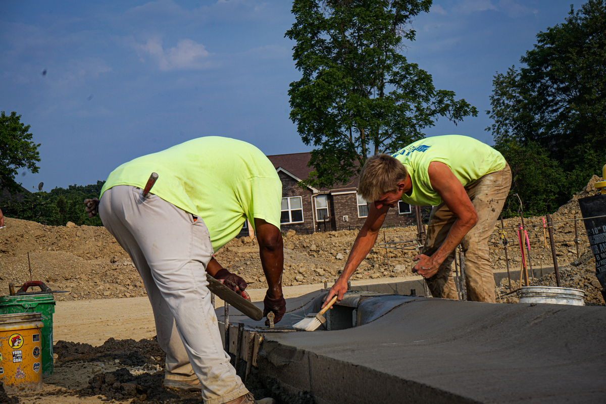 Two construction workers smoothing freshly poured concrete at a job site.